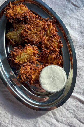 Potato latkes on a platter with a small dish of sour cream.