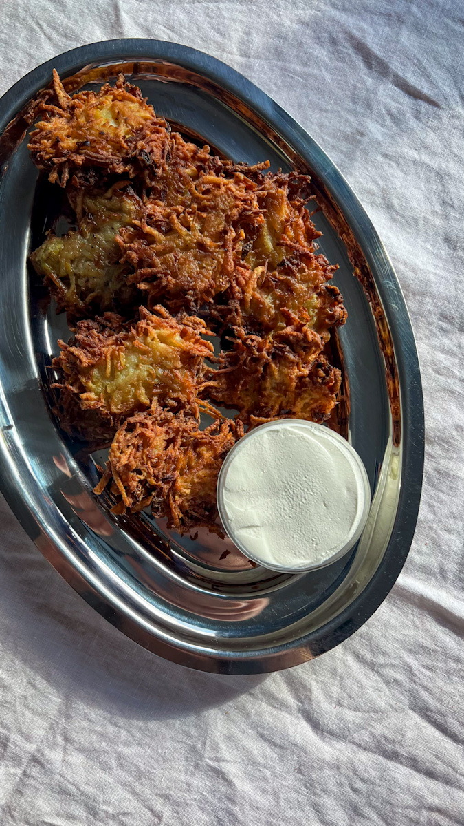 Potato latkes on a platter with a small dish of sour cream.