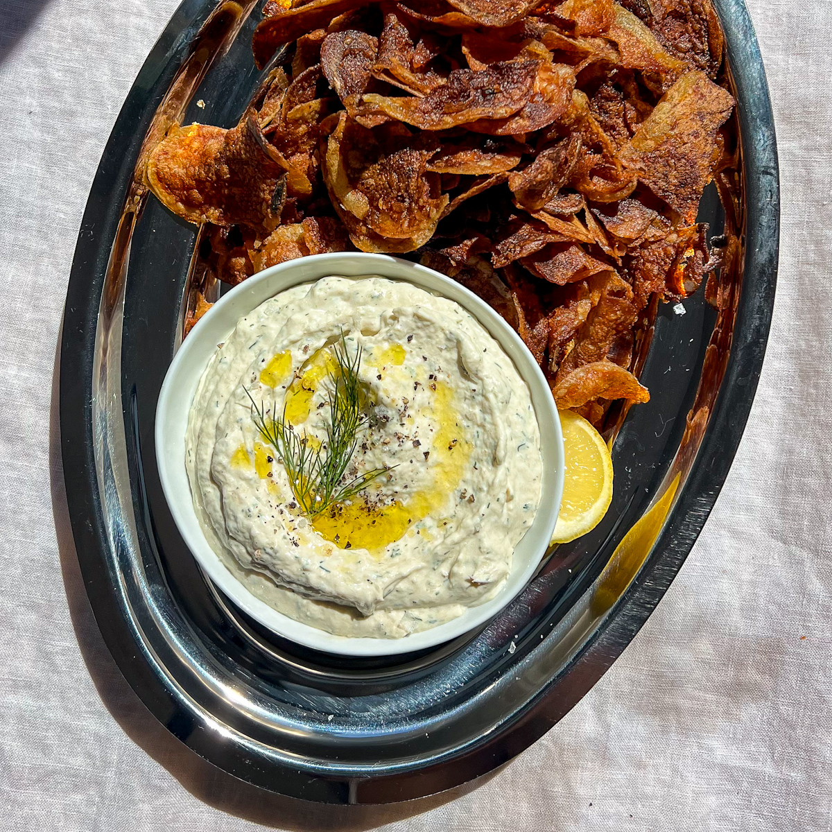 Creamy horseradish smoked trout dip topped with fresh dill and black pepper on a silver platter.